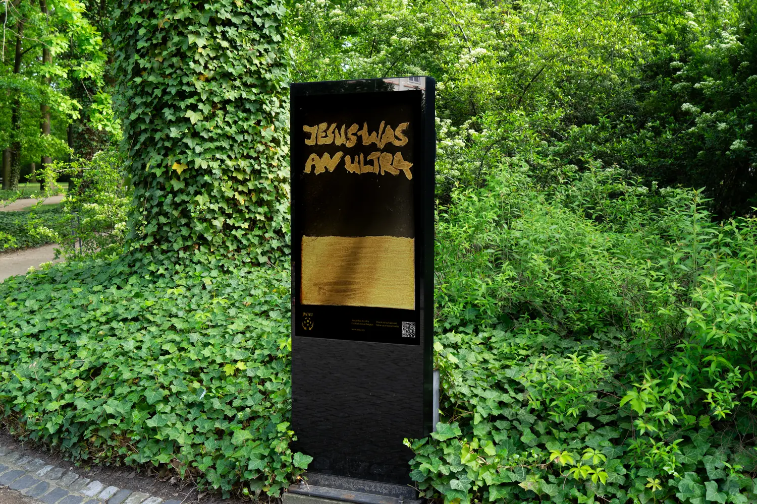 A digital billboard in a park path carrying the gold Jesus Was An Ultra graffiti